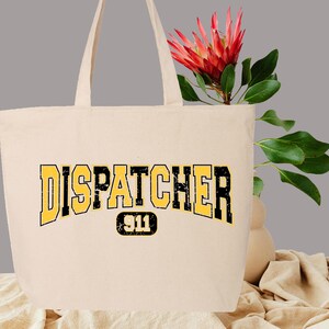 May include: A beige tote bag with black and yellow text that reads "DISPATCHER 911". The text is in a vintage collegiate font.