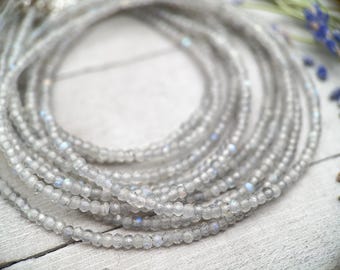May include: A close-up of a multi-strand necklace made of small, iridescent, gray beads. The necklace is lying on a white surface.