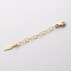 May include: Gold chain extender with a leaf charm. The extender is approximately 2 inches long and has a lobster clasp.