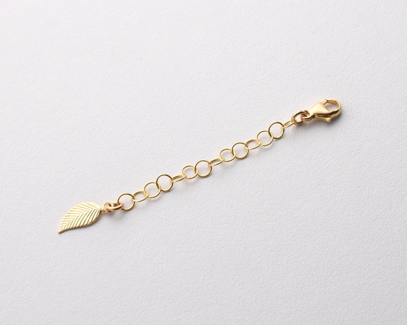 May include: Gold chain extender with a leaf charm. The extender is approximately 2 inches long and has a lobster clasp.
