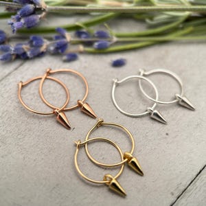 May include: Three pairs of hoop earrings with pointed ends. The earrings are in gold, rose gold, and silver.