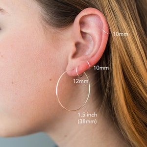 May include: Three silver hoop earrings in different sizes. The largest hoop is 1.5 inches (38mm) in diameter, the middle hoop is 12mm in diameter, and the smallest hoop is 10mm in diameter.