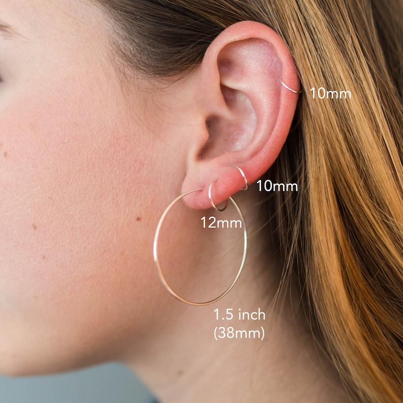 May include: Three silver hoop earrings in different sizes. The largest hoop is 1.5 inches (38mm) in diameter, the middle hoop is 12mm in diameter, and the smallest hoop is 10mm in diameter.