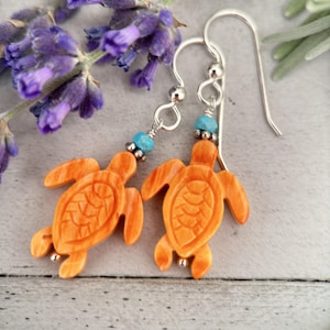 May include: A pair of silver dangle earrings featuring carved orange turtle charms with turquoise beads.