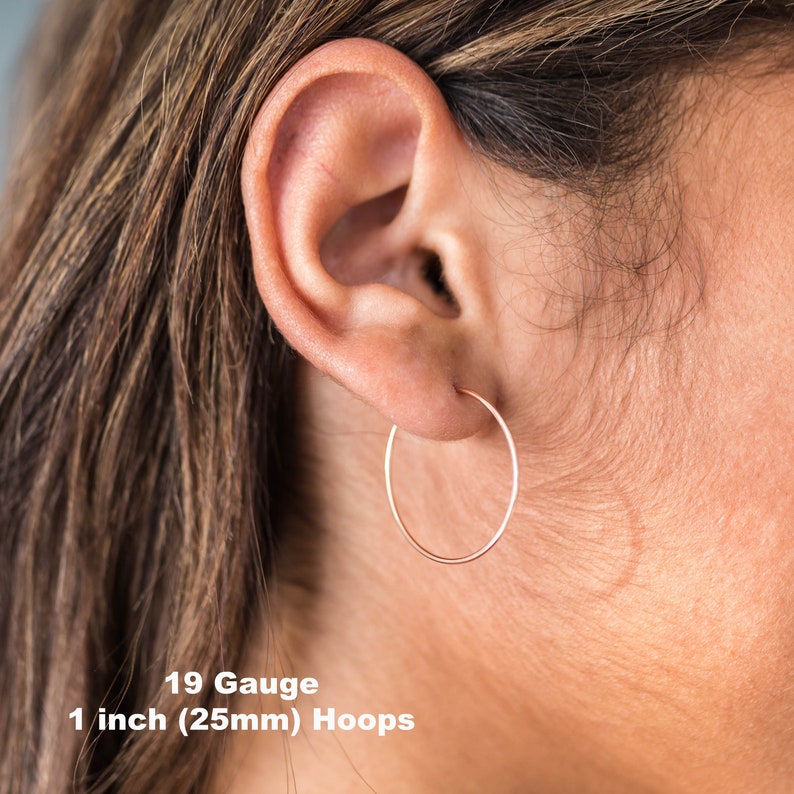 May include: A close-up of a person's ear wearing a thin, rose gold hoop earring. The text on the image reads "19 Gauge 1 inch (25mm) Hoops". The earring is a simple, circular design.