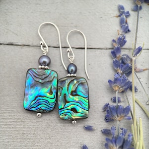 May include: A pair of silver earrings with iridescent abalone shell and black pearl accents.