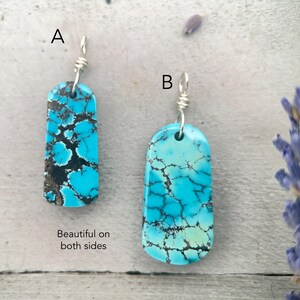 May include: Two turquoise stone pendants with silver wire loops. The rectangular stones have a vibrant blue colour with dark brown veining. The text "Beautiful on both sides" is visible.