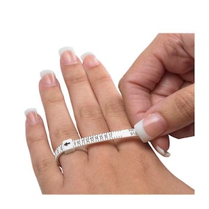 May include: White plastic ring sizer with black markings from size 9 to 17. The sizer is being used to measure a finger.