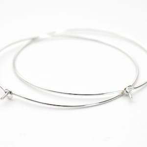 Op de afbeelding: Twee zilverkleurige oorringen van draad met een eenvoudig, minimalistisch ontwerp. Elke oorring heeft een kleine, geluste sluiting. De oorbellen staan tegen een effen witte achtergrond, wat hun delicate structuur benadrukt.