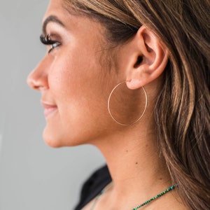 May include: Rose gold hoop earrings. The earrings are large, circular, and made of a shiny, metallic material. The hoops are worn on the ear of a person.