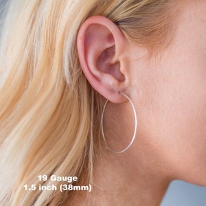 Op de afbeelding: Close-up van een oor met een zilveren oorring. De oorring heeft een diameter van 38 mm en is 19 gauge. Blond haar. Tekst: 19 Gauge 1.5 inch (38mm).