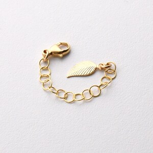 May include: Gold chain extender with a leaf charm. The extender has a lobster clasp and is made of gold-toned metal.