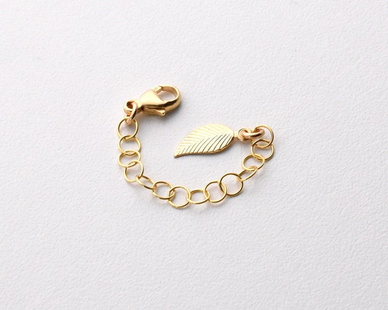 May include: Gold chain extender with a leaf charm. The extender has a lobster clasp and is made of gold-toned metal.