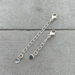 May include: Two silver chain extenders with heart-shaped charms. Each extender has a lobster clasp on one end and a heart charm on the other.