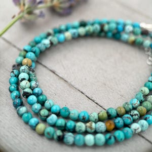 Könnte beinhalten: Nahaufnahme von drei Strängen türkisfarbener Perlenketten. Die Perlen sind eine Mischung aus blau-grünen Farbtönen mit braunen und schwarzen Matrixmustern. Die Halsketten sind geschichtet, mit einem silbernen Verschluss.