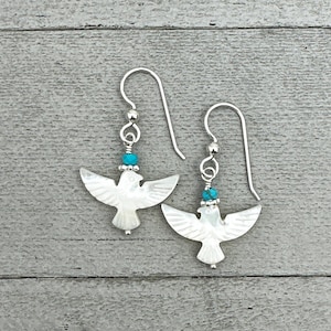 May include: A pair of silver earrings featuring a white mother of pearl bird design with a turquoise bead accent.