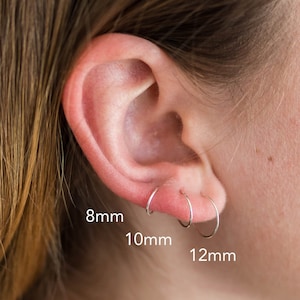 May include: Three silver hoop earrings in different sizes: 8mm, 10mm, and 12mm. The earrings are shown in a person's ear.