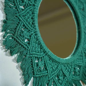 May include: A green macrame mirror with a circular frame. The frame is made of knotted yarn with a fringe around the edge.