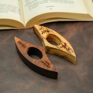 May include: Two wooden thumb page holders. One is dark brown with the name "Rachel" engraved, and the phrase "a new chapter begins..." The other is light brown with floral designs and the letter "V".