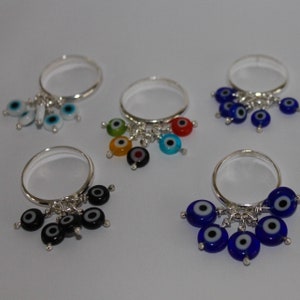 May include: Five silver rings with dangling evil eye charms. Each ring has five charms in different colors, including blue, green, red, black, and white.