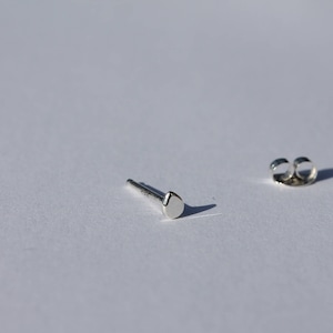 May include: A pair of silver stud earrings with a small, round, flat design. The earrings are on a white background.