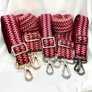 May include: A collection of burgundy and pink woven bag straps with silver and gold-colored metal hardware. The straps have a geometric pattern and are designed for use with handbags or other accessories. The image shows several straps and matching wristlets.