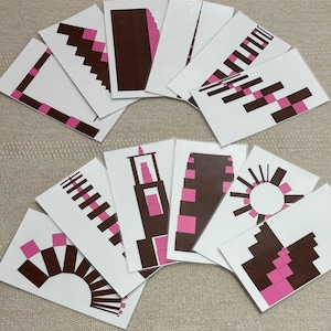 May include: A set of 12 cards with different patterns of brown and pink blocks. The cards are arranged in a semi-circle on a beige surface.