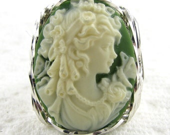 May include: A white cameo ring with a green background. The cameo features a woman's profile with a floral design.