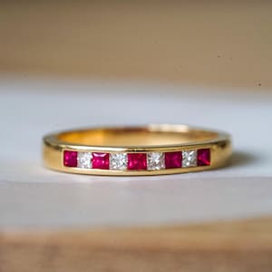 Puede incluir: Un anillo de banda de oro con una fila de rubíes rojos y diamantes transparentes alternados.