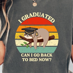 Puede incluir: Una camiseta gris con un gráfico de estilo vintage de un perezoso con un gorro de graduación. El texto en la camiseta dice "I Graduated Can I Go Back To Bed Now?"