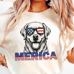 Könnte beinhalten: Sandfarbenes T-Shirt mit einer Grafik eines Hundes mit Sonnenbrille im Design der amerikanischen Flagge. Das Wort "MERICA" ist in Rot, Weiß und Blau gedruckt. Das Model trägt eine hellblaue Jeans.