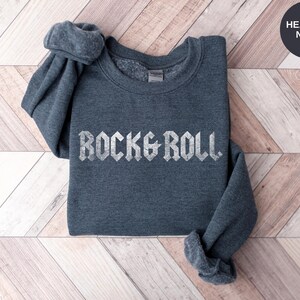 Puede incluir: Sudadera azul marino jaspeada con el texto "Rock & Roll" en blanco, en una fuente desgastada.