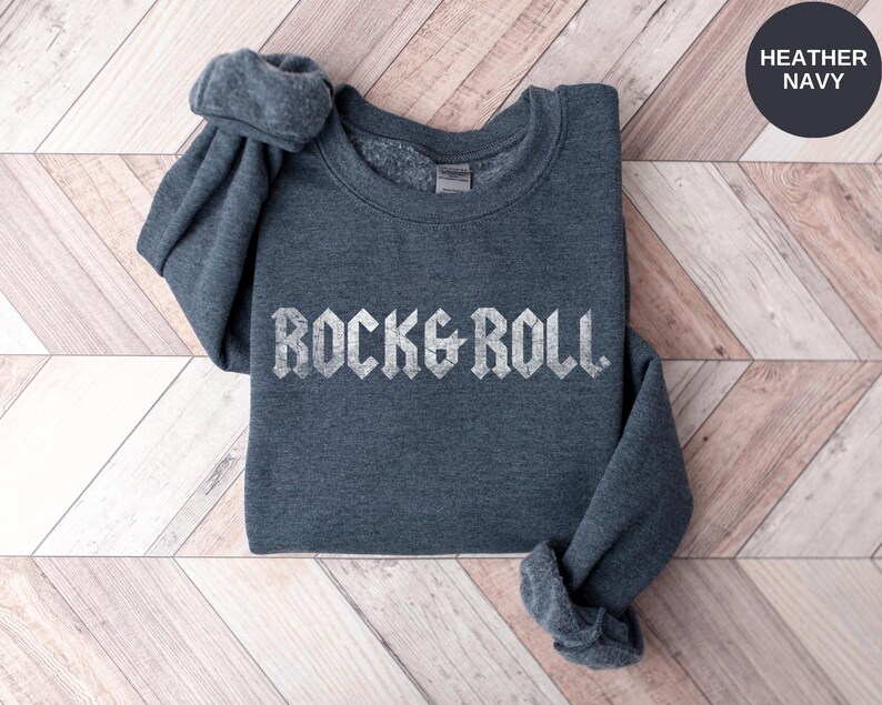 Puede incluir: Sudadera azul marino jaspeada con el texto "Rock & Roll" en blanco, en una fuente desgastada.