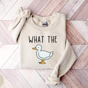 May include: A sand-colored sweatshirt with the text "WHAT THE" and a cartoon duck illustration.