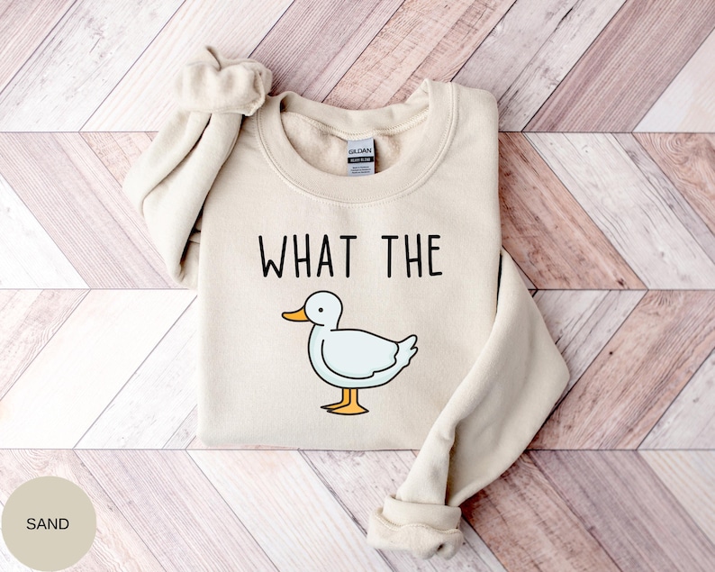 May include: A sand-colored sweatshirt with the text "WHAT THE" and a cartoon duck illustration.