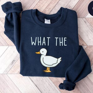 May include: A navy blue sweatshirt with the text "WHAT THE" printed in white and a cartoon duck illustration.
