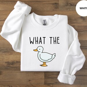 May include: White crewneck sweatshirt with the text "WHAT THE" and a cartoon duck illustration.