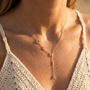 May include: A gold-toned necklace featuring the name Sophia spelled out in individual capital letters. The letters S, O, P, H, I, and A are arranged in a vertical and diagonal pattern along the delicate chain, creating a personalized jewelry piece.