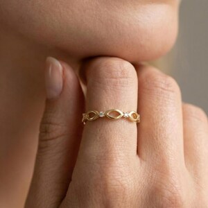 May include: A gold ring featuring an open oval pattern, set with tiny, clear gemstones. The ring is displayed on a finger, emphasizing its delicate and elegant design. The warm gold hue of the ring contrasts with the skin, highlighting its intricate details.