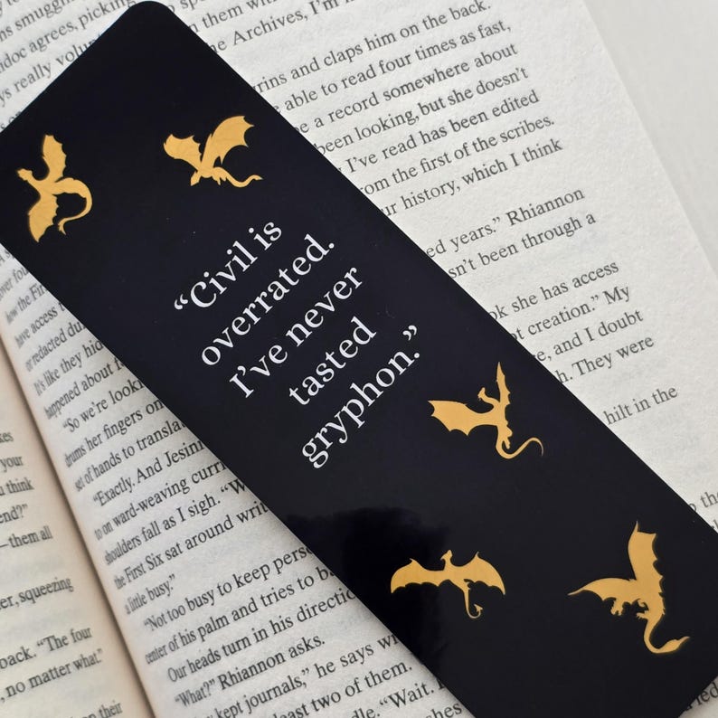 May include: Black bookmark featuring gold dragon silhouettes and the quote "Civil is overrated. I've never tasted gryphon."
