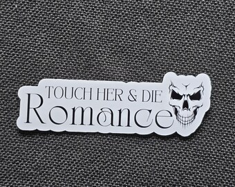 May include: A white sticker featuring the words "TOUCH HER & DIE Romance" and a skull illustration. The sticker is rectangular with rounded corners and is set against a textured grey background.