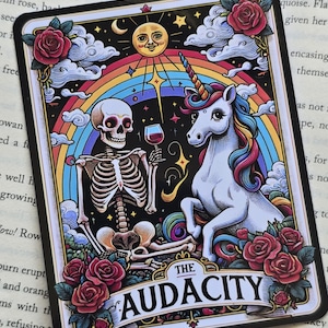 May include: A tarot card with a black background and a rainbow arch. The card features a skeleton and a unicorn drinking wine together. The card is titled "The Audacity".