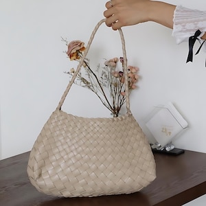 May include: A beige woven leather tote bag with a braided strap. The bag is made of a soft, supple leather and has a spacious interior.