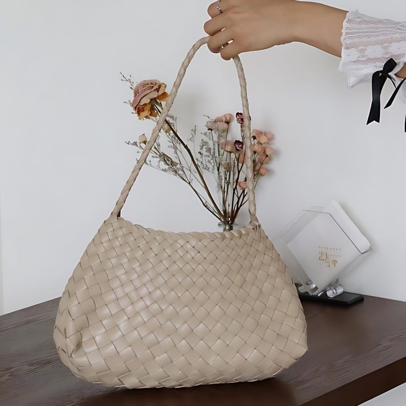 May include: A beige woven leather tote bag with a braided strap. The bag is made of a soft, supple leather and has a spacious interior.