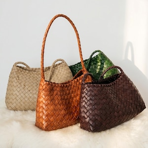 Peut inclure: Quatre sacs à bandoulière tressés en beige, fauve, vert foncé et marron foncé. Chaque sac présente un motif entrelacé uniforme sur tout le corps et une seule bandoulière tressée. Les sacs sont disposés en groupe à des hauteurs variées.