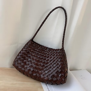 May include: A brown woven leather handbag with a single strap. The bag has a rectangular shape with a slightly curved bottom.
