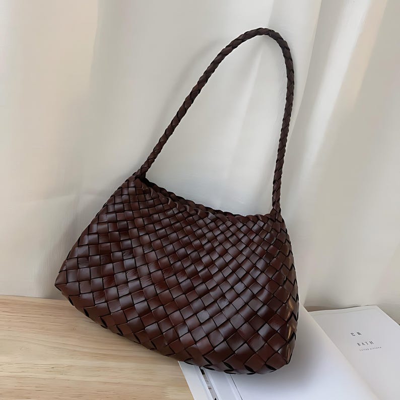 May include: A brown woven leather handbag with a single strap. The bag has a rectangular shape with a slightly curved bottom.