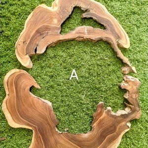Pode incluir: Duas placas de madeira inacabadas de forma irregular, com bordas naturais e uma rica cor marrom. As placas têm padrões de grãos únicos e formas orgânicas, com a letra "A" visível entre elas. A madeira está sobre um fundo verde.