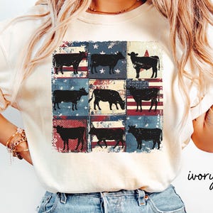 May include: Ivory-colored t-shirt featuring a grid of nine squares, each with a silhouette of a cow against a backdrop of the American flag. The word "ivory" is written in cursive on the lower right.