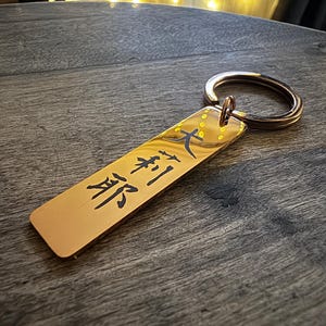 以下が含まれることがあります： 日本語の文字が刻まれた長方形のタグが付いた金色のキーホルダー。タグには「大将」と書いてあり、これは「司令官」を意味します。
